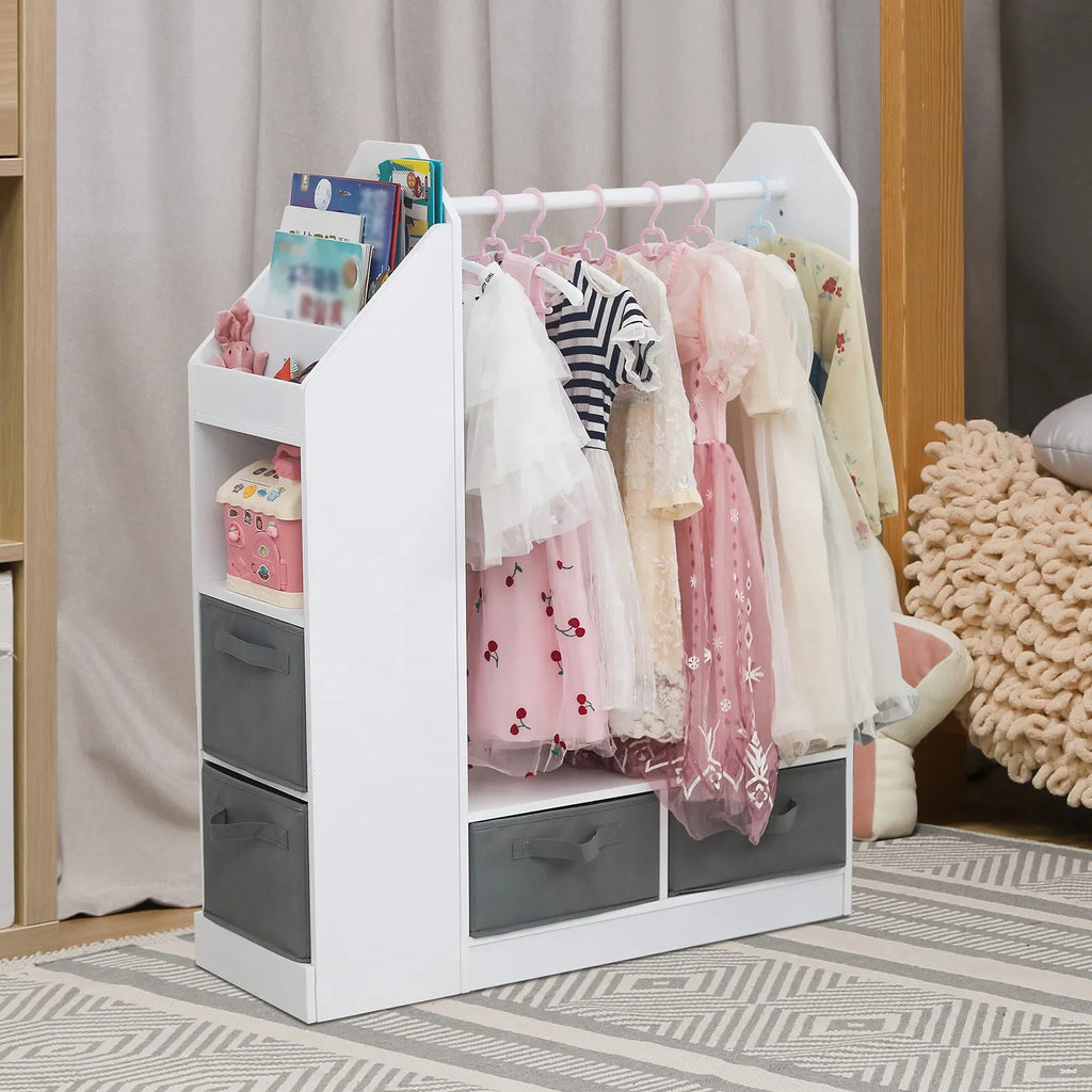 A white children's clothing rack organizer with gray storage drawers, shown holding several pastel dresses and holding books in its side shelves, placed in a bedroom setting.